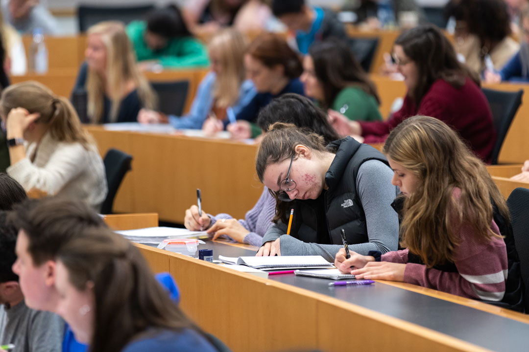 Students handwriting notes in a crowded classroom